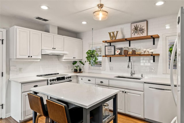 kitchen with visible vents, range with electric cooktop, dishwashing machine, under cabinet range hood, and a sink