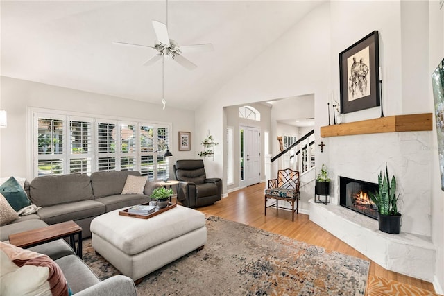 living room with high vaulted ceiling, light wood-style flooring, a fireplace, a ceiling fan, and baseboards