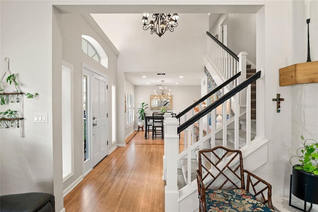 foyer entrance featuring visible vents, a towering ceiling, an inviting chandelier, stairs, and light wood-type flooring