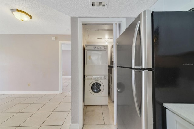 laundry area featuring light tile patterned flooring, stacked washer and dryer, and a textured ceiling