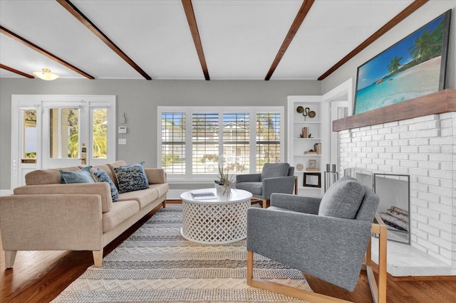 living room with hardwood / wood-style flooring, beamed ceiling, and a brick fireplace