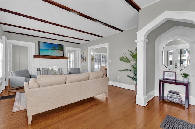 living room featuring beamed ceiling, wood-type flooring, ornate columns, and a fireplace