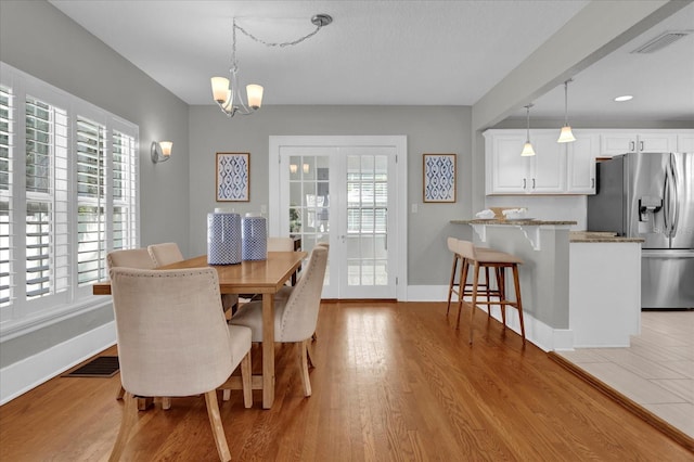 dining area with a healthy amount of sunlight, french doors, light hardwood / wood-style floors, and a notable chandelier