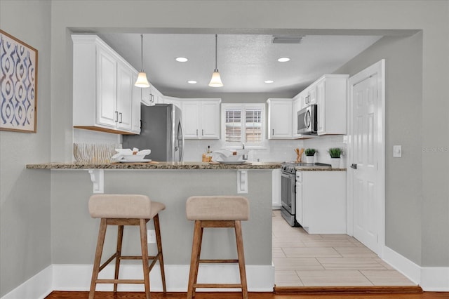 kitchen featuring stainless steel appliances, white cabinets, decorative light fixtures, light stone countertops, and kitchen peninsula