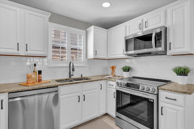 kitchen with white cabinetry, appliances with stainless steel finishes, decorative backsplash, light stone countertops, and sink