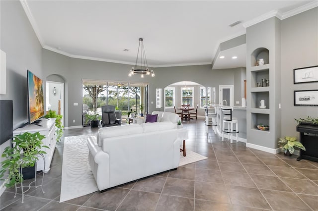 living room featuring tile patterned floors, crown molding, built in shelves, and a notable chandelier