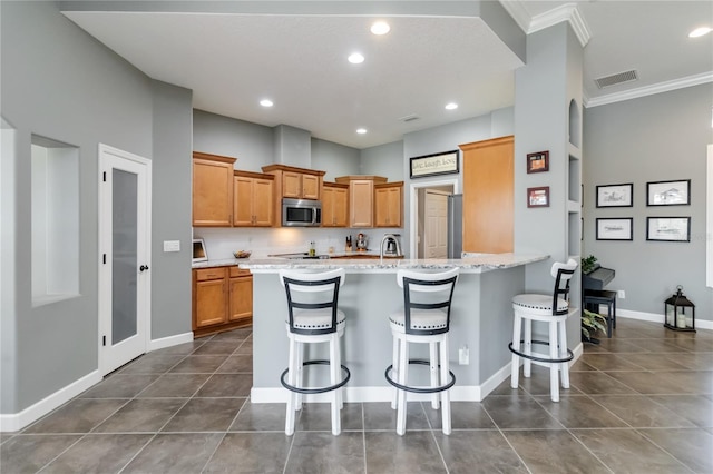 kitchen featuring kitchen peninsula, light stone countertops, dark tile patterned flooring, crown molding, and a kitchen breakfast bar