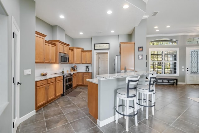 kitchen with appliances with stainless steel finishes, tasteful backsplash, dark tile patterned flooring, light stone countertops, and a breakfast bar