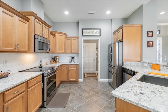 kitchen featuring sink, light stone counters, light tile patterned floors, appliances with stainless steel finishes, and decorative backsplash