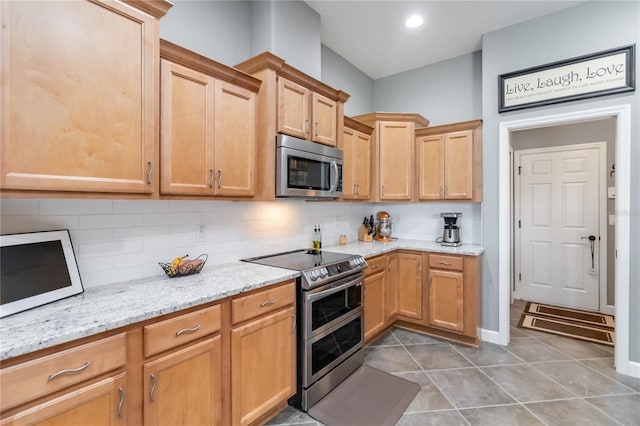 kitchen featuring appliances with stainless steel finishes, dark tile patterned flooring, light stone countertops, and tasteful backsplash