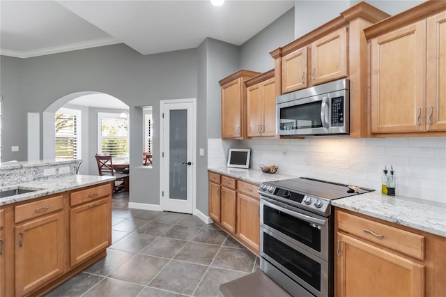 kitchen with dark tile patterned flooring, light stone counters, stainless steel appliances, and decorative backsplash