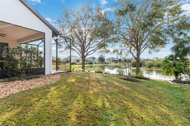 view of yard with a water view, ceiling fan, and a lanai