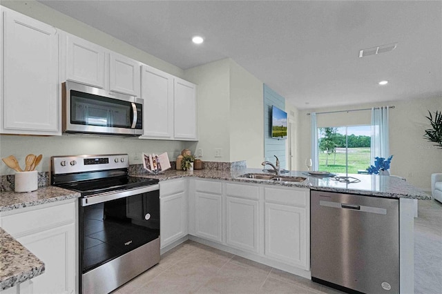 kitchen with appliances with stainless steel finishes, sink, kitchen peninsula, white cabinets, and light stone countertops