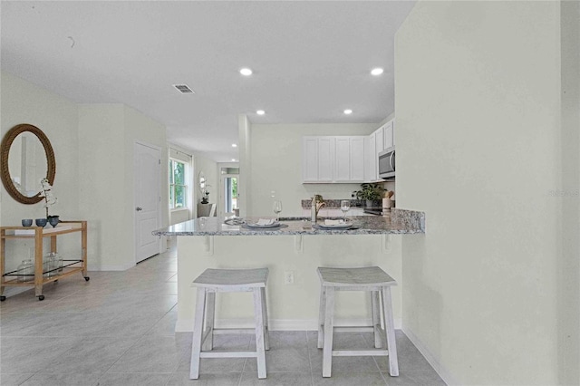 kitchen with stone countertops, a kitchen breakfast bar, white cabinets, light tile patterned floors, and kitchen peninsula