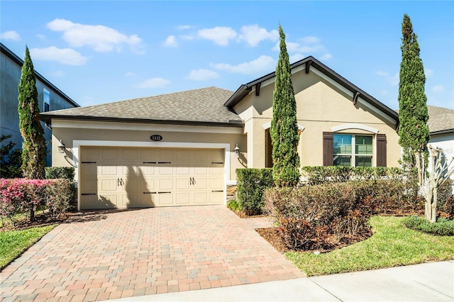 ranch-style home featuring decorative driveway, roof with shingles, an attached garage, and stucco siding