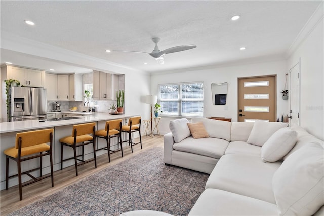 living room with hardwood / wood-style flooring, a textured ceiling, ceiling fan, crown molding, and sink