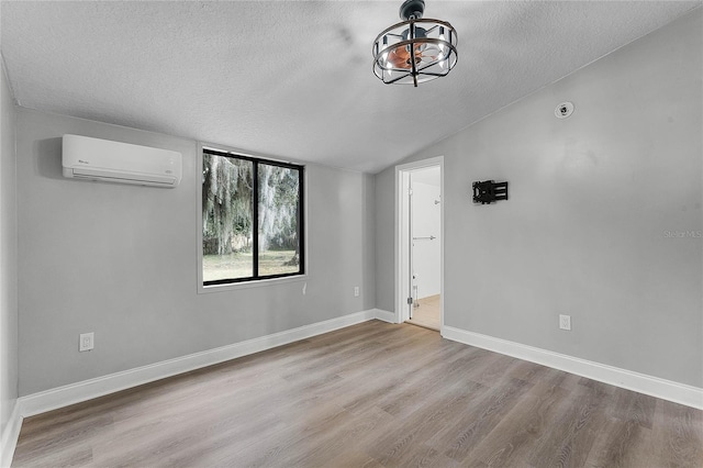 empty room featuring lofted ceiling, light hardwood / wood-style floors, a textured ceiling, and a wall mounted air conditioner