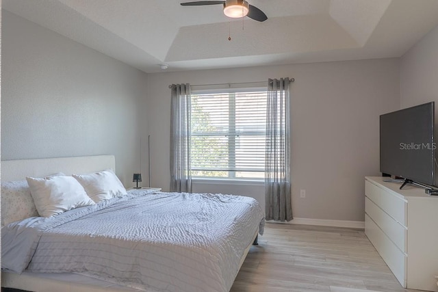 bedroom with light wood finished floors, baseboards, a tray ceiling, and ceiling fan