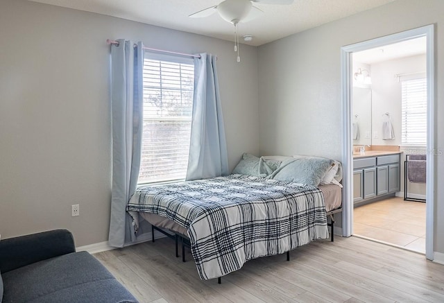 bedroom featuring light wood finished floors, a sink, ceiling fan, ensuite bath, and baseboards