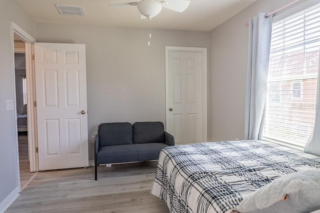 bedroom with a ceiling fan, light wood-style flooring, visible vents, and baseboards