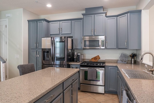 kitchen featuring light tile patterned floors, stainless steel appliances, gray cabinetry, a sink, and light stone countertops