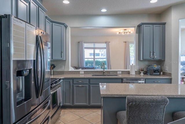 kitchen featuring stainless steel appliances, gray cabinets, a sink, and light stone countertops