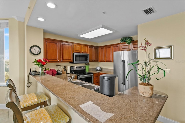 kitchen featuring a peninsula, a breakfast bar, stainless steel appliances, a sink, and visible vents