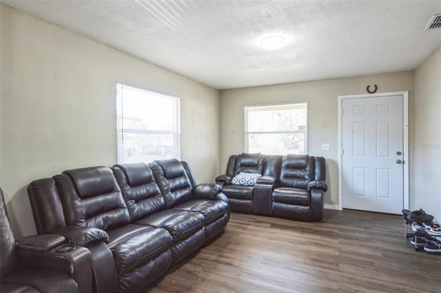 living area featuring a textured ceiling, dark wood-type flooring, plenty of natural light, and visible vents