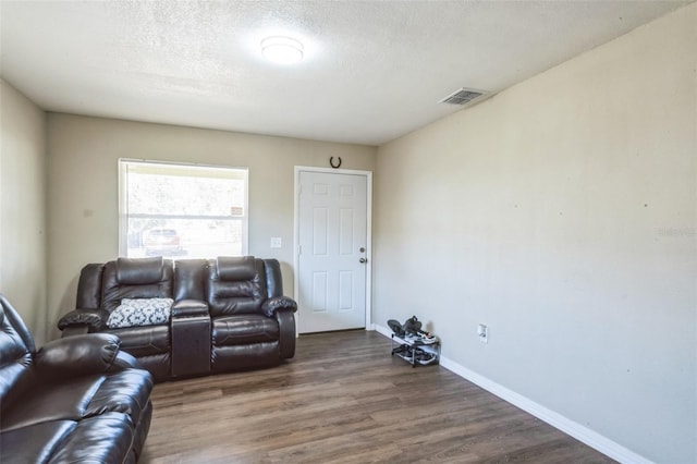 living room featuring baseboards, a textured ceiling, visible vents, and dark wood-style flooring