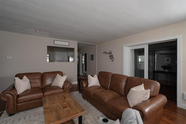 living room featuring light wood-type flooring, a wall unit AC, and a textured ceiling