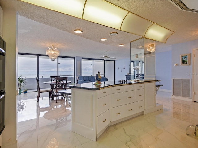 kitchen with dark stone counters, a kitchen island, a textured ceiling, white cabinets, and ceiling fan with notable chandelier