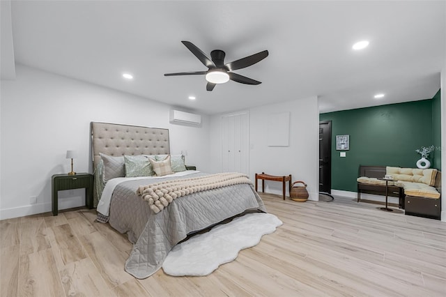 bedroom with a wall mounted air conditioner, light wood-type flooring, and ceiling fan