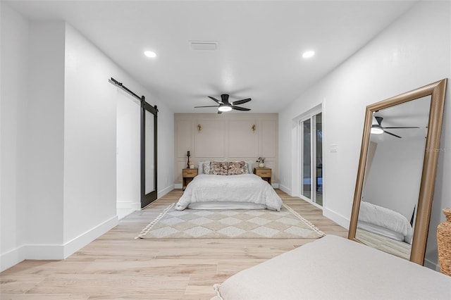 bedroom featuring light wood-type flooring, multiple closets, ceiling fan, and a barn door