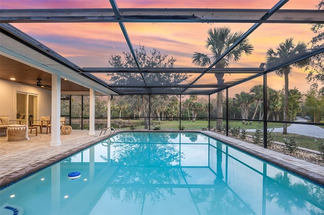 pool at dusk featuring a patio area, an outdoor living space, ceiling fan, and a lanai