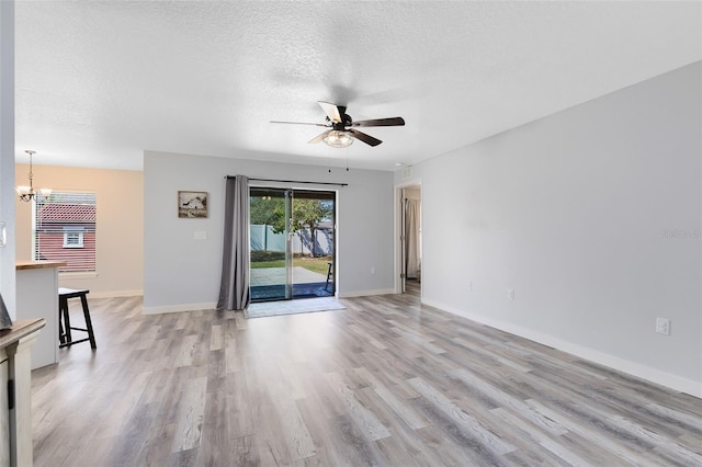 unfurnished living room with ceiling fan with notable chandelier, light hardwood / wood-style floors, and a textured ceiling