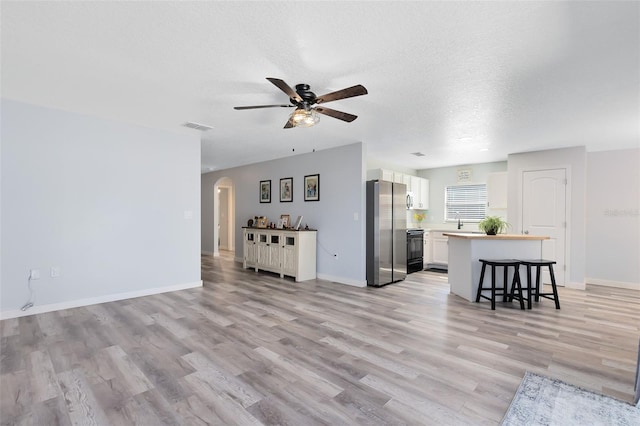 living room with a textured ceiling, ceiling fan, and light hardwood / wood-style flooring