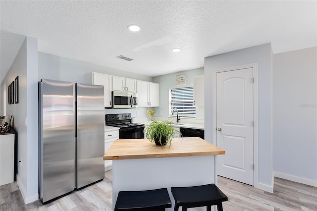 kitchen with light hardwood / wood-style flooring, a center island, white cabinetry, butcher block countertops, and black appliances