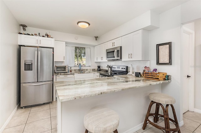 kitchen with light stone counters, stainless steel appliances, a peninsula, a sink, and white cabinets