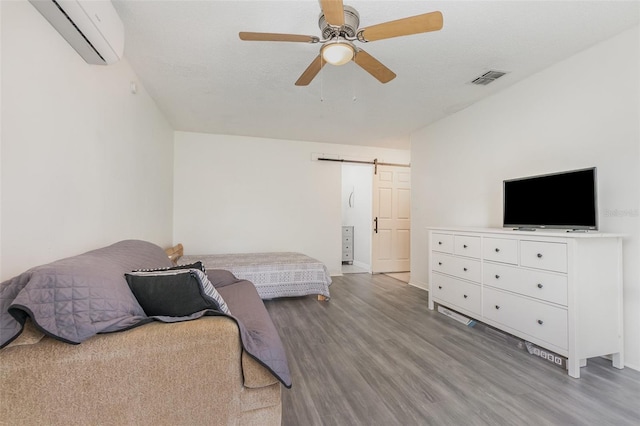 bedroom with a barn door, a wall unit AC, light wood-style flooring, visible vents, and a ceiling fan