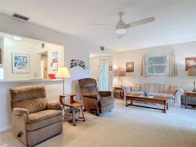 living room with a ceiling fan, visible vents, light carpet, and a textured ceiling