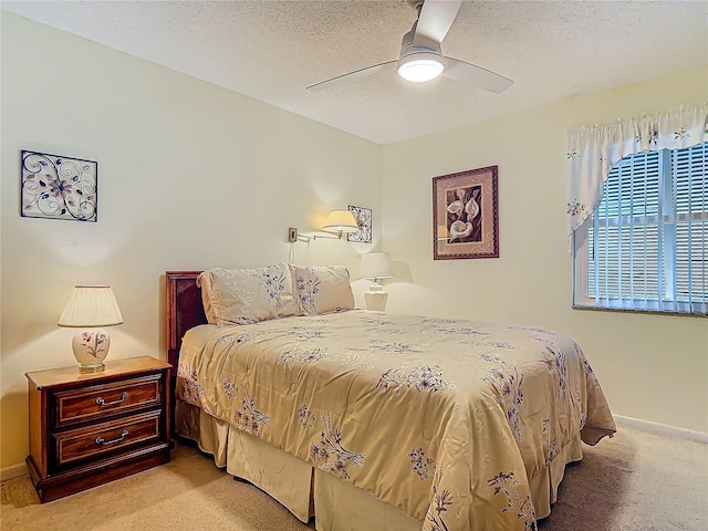 bedroom with light carpet, a textured ceiling, a ceiling fan, and baseboards