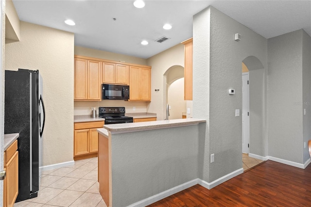 kitchen featuring light wood-type flooring, kitchen peninsula, black appliances, sink, and light brown cabinetry