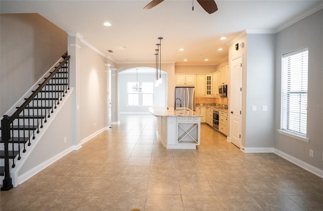 kitchen with light stone counters, pendant lighting, stainless steel appliances, glass insert cabinets, and an island with sink