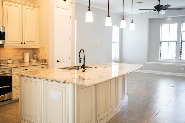 kitchen featuring a kitchen island with sink, decorative light fixtures, a sink, and cream cabinets