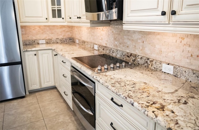 kitchen featuring appliances with stainless steel finishes, light tile patterned flooring, glass insert cabinets, and white cabinetry