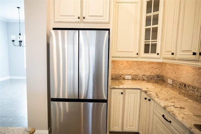 kitchen with decorative backsplash, glass insert cabinets, freestanding refrigerator, hanging light fixtures, and light stone countertops