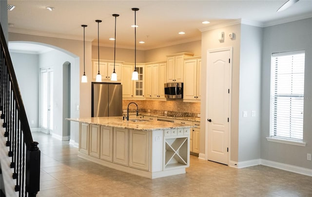 kitchen with arched walkways, a center island with sink, appliances with stainless steel finishes, glass insert cabinets, and a sink