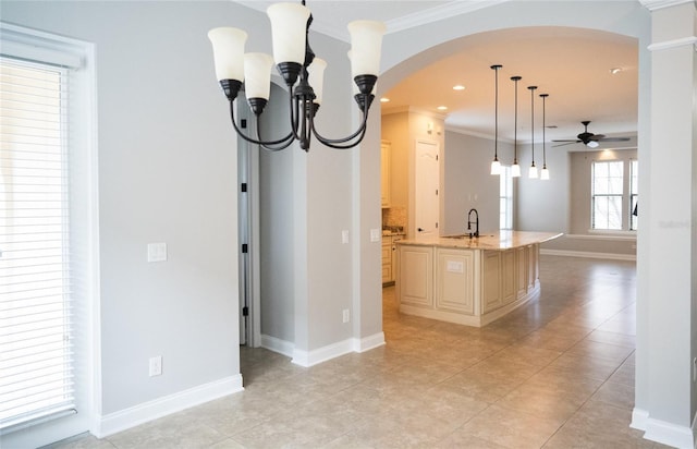 kitchen featuring light stone counters, arched walkways, a center island with sink, ornamental molding, and a sink