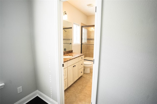 bathroom featuring toilet, vanity, baseboards, tile patterned floors, and a shower with door