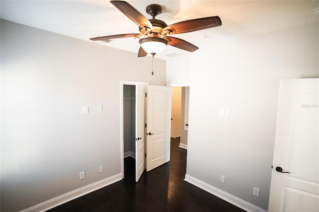 unfurnished bedroom featuring dark wood-style floors, a spacious closet, ceiling fan, and baseboards